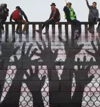 Hands reaching at border fence, migrants sitting on border wall, faded US flag