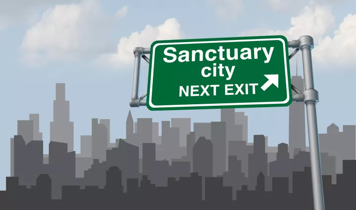 sanctuary city sign in front of a city skyline
