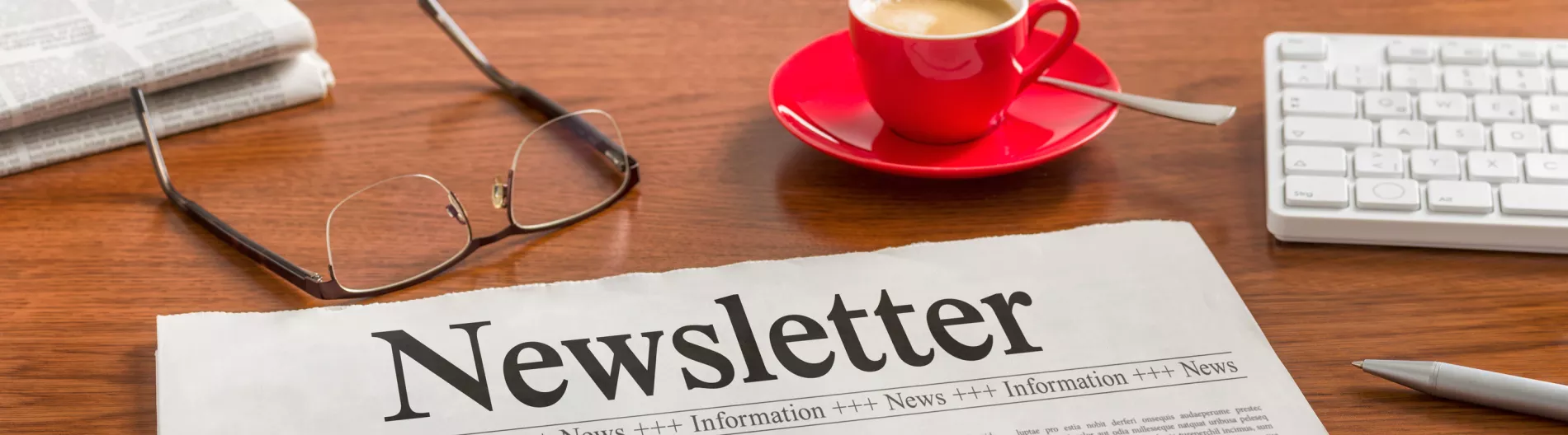 Newsletter on top of a desk with eyeglasses and cup of coffee