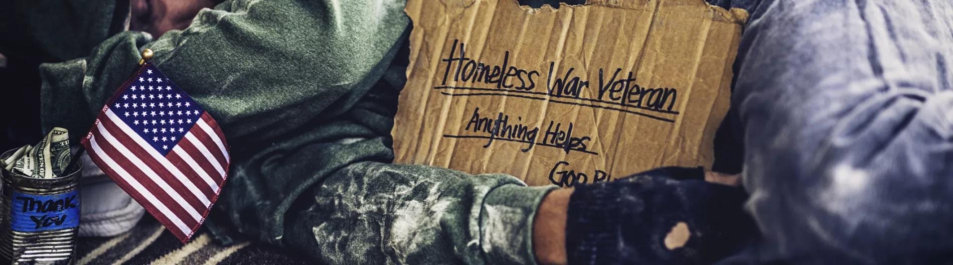 Homeless war veteran sleeping with sign and money tin