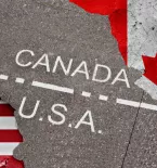 U.S. and Canadian Flags on Cracked Asphault with "CANADA" and "U.S.A." written on one side or the other of a marked border