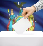 Hand putting card in ballot box with New York flag in background