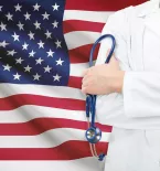 Man in doctor's coat holding stethoscope in from of American flag