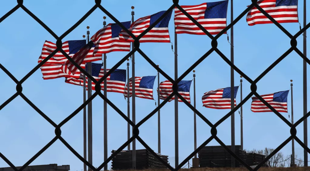 Image of multiple U.S. flags behind metal border fence